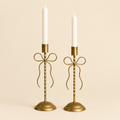 Set of two gold bow taper candle holders on a cream background