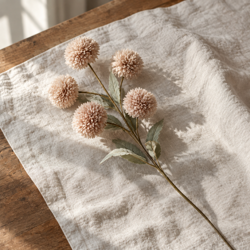 Single blush pompom faux flower stem on cream linen